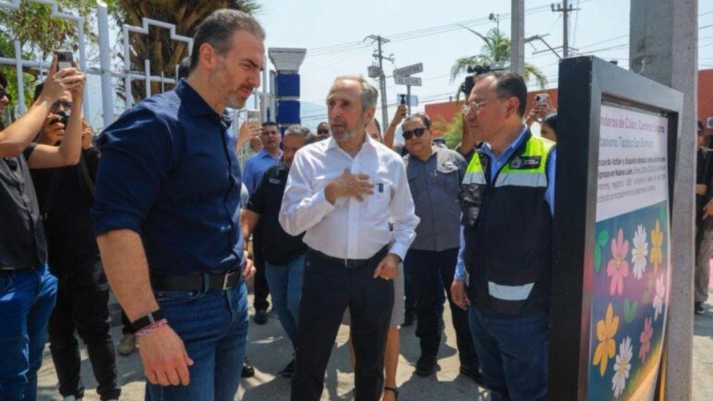 Group of men some in uniforms stand outdoors around a flower themed information panel listening to a speaker   Informe Regio