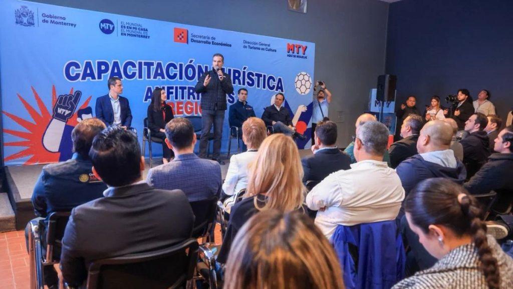 Speaker on stage at a tourism training conference with panelists and a blue banner reading CAPACITACIÓN TURÍSTICA behind them audience seated in front   Informe Regio