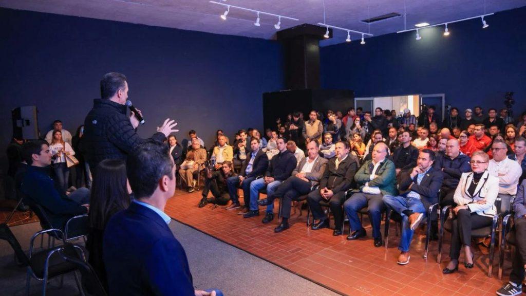 Speaker with microphone addressing a large audience in a dimly lit conference room on a stage left platform   Informe Regio