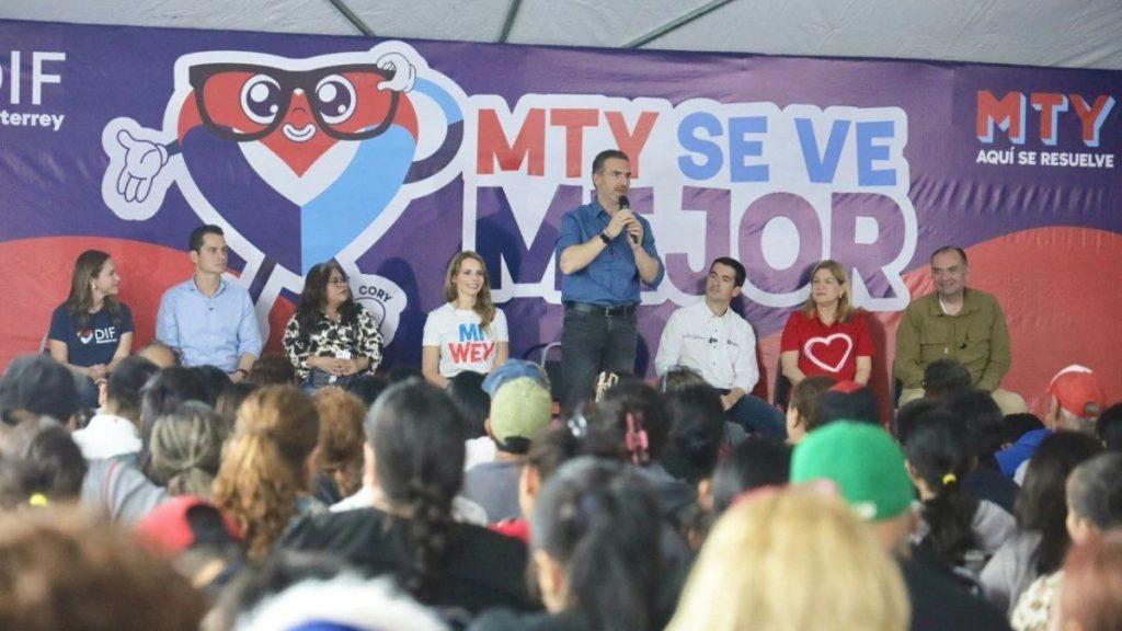 Panel of eight people seated on a stage during a community event with a large purple banner and crowd in the foreground   Informe Regio