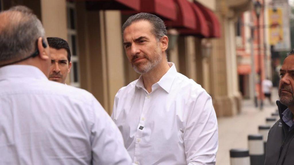 Man in a white shirt talking with two other men on a city sidewalk near storefronts with red awnings   Informe Regio
