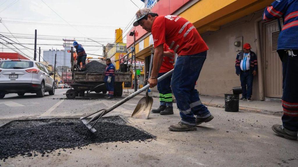 Workers repair a pothole on a city street one man shoveling asphalt while others stand nearby   Informe Regio