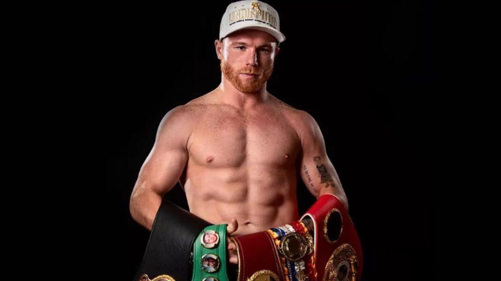 Male shirtless boxer wearing a light colored cap posing with multiple boxing championship belts against a black background   Informe Regio