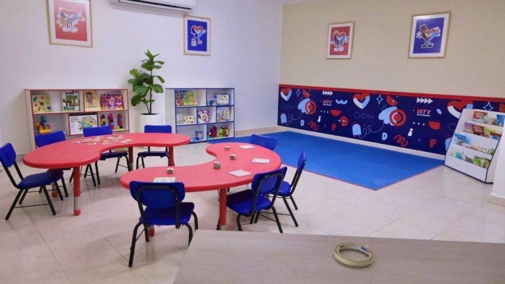 A bright childrens playroom with red curved tables blue chairs and shelves of toys and books against white walls   Informe Regio