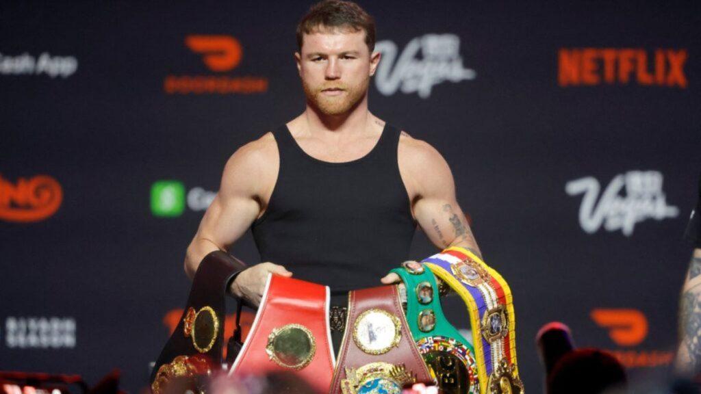Boxer in a black sleeveless shirt on stage draped with multiple championship belts around his waist and shoulder posing for photos   Informe Regio