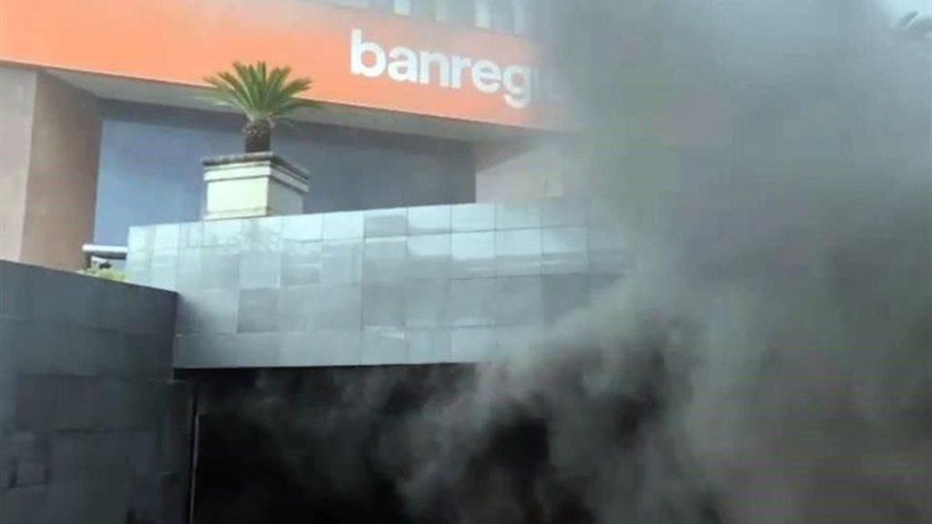 Smoke rising from a doorway of a modern building with an orange sign reading banreg above it   Informe Regio