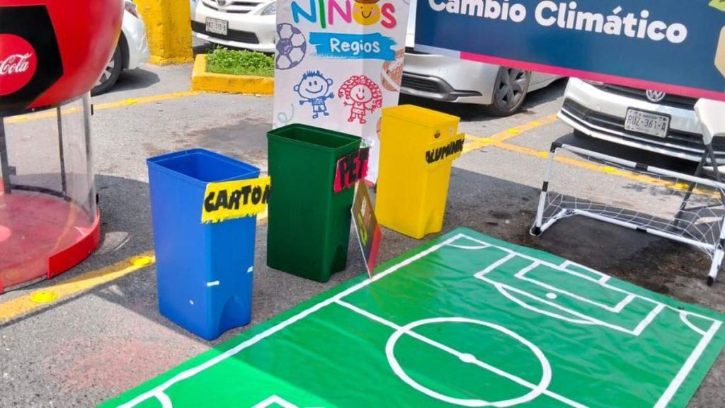 Blue carton recycling bin green and yellow waste bins labeled for different waste beside a green football field mat and a climate change banner   Informe Regio