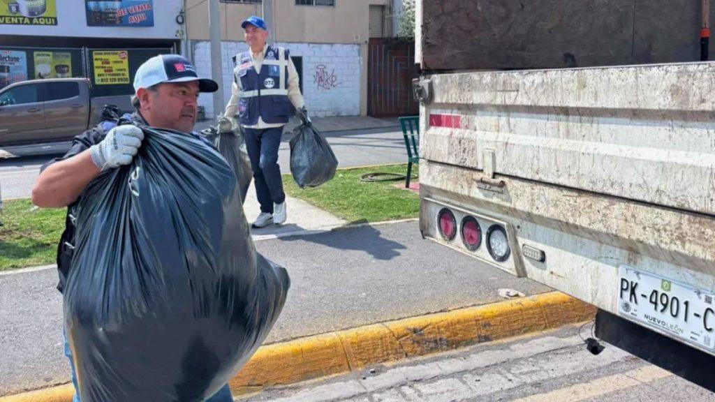 Man in a cap lifts a large black garbage bag beside a parked truck on a city street as another worker carries bags in the background   Informe Regio