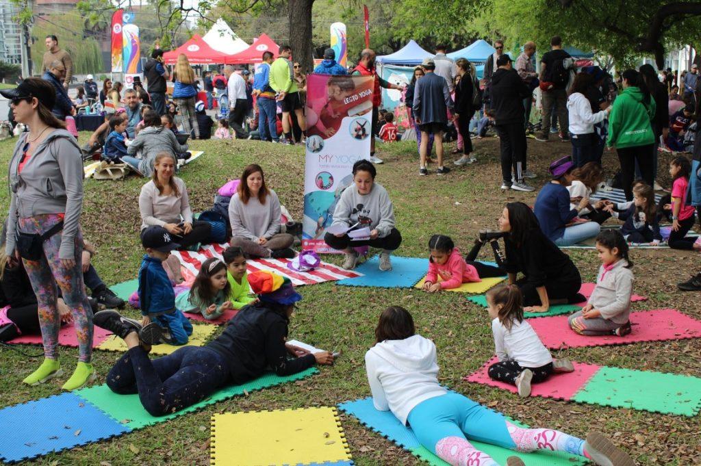 Children and adults doing yoga on colorful mats in a park during a community event with tents in the background   Informe Regio