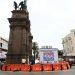 Tall stone monument rising from a traffic circle surrounded by bright orange barrier blocks and a large billboard that reads Vialidades Régias   Informe Regio