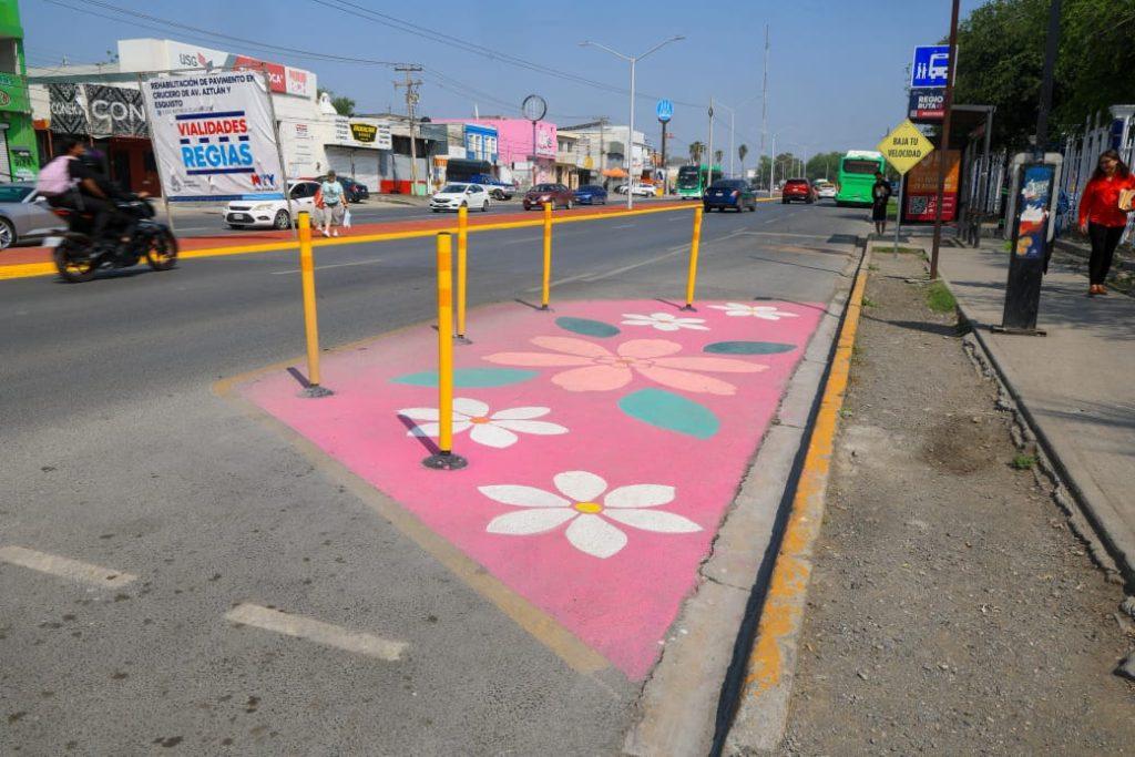 Painted pink pedestrian refuge island with white flowers and yellow bollards along a busy street   Informe Regio
