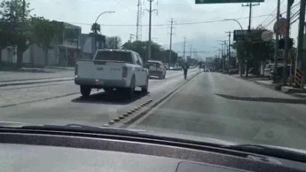 View from a car white pickup truck in the left lane ahead on a city street with a rider in the middle lane and power lines along the road   Informe Regio