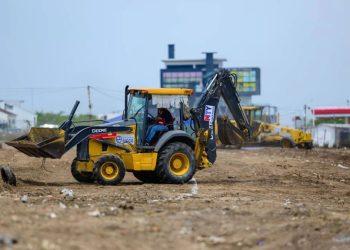 Yellow backhoe loader at a dirt construction site, scooping soil with other heavy machinery in the background