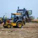 Yellow backhoe loader at a dirt construction site scooping soil with other heavy machinery in the background   Informe Regio