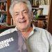 Older man with gray hair smiles at the camera while holding a book titled GRANDES TEXTOS   Informe Regio