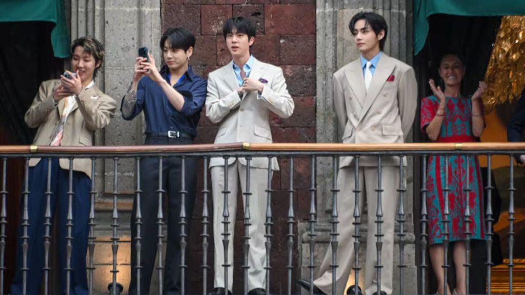 Four men in suits on a balcony two are taking photos with their phones while others watch the event with a woman in a colorful dress clapping on the right   Informe Regio