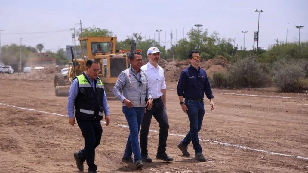 Four men walk together on a dirt construction site with heavy machinery in the background wearing work vests and casual shirts   Informe Regio