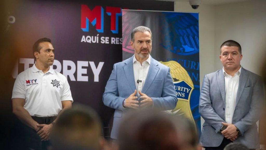Adrián-de-la-garza-curso-táctico-eventos-masivos - Informe Regio Three men on a stage during a briefing the central man in a light blue suit speaks while two others stand nearby with a security themed backdrop behind them Informe Regio