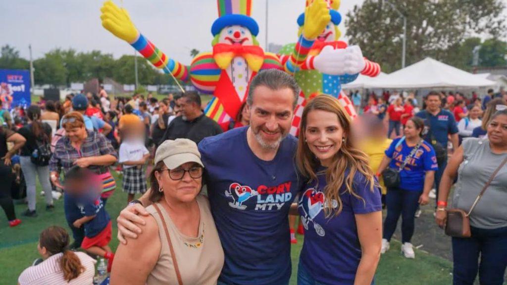 Group of three people posing for a photo at a crowded outdoor festival with large inflatable clowns in the background   Informe Regio