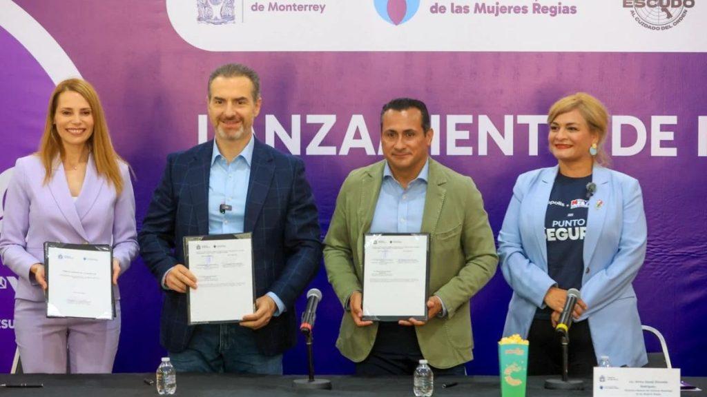 Four professionals stand behind a table each holding framed documents at a formal signing ceremony against a purple backdrop with logos and text A microphone and water bottle are on the table   Informe Regio