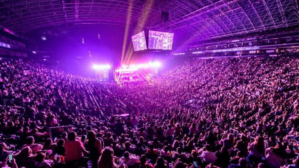 Packed arena concert with a bright purple lit stage and a sea of fans watching the performance from all levels   Informe Regio