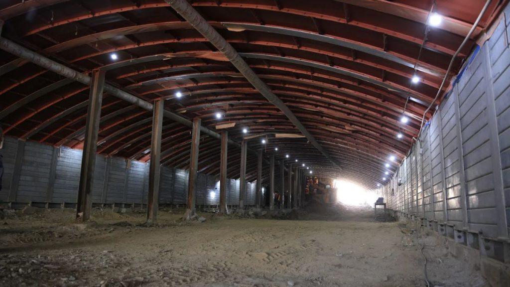 Av-acueducto-circuito-vial-huajuco-monterrey-tunel - Informe Regio Long dim tunnel inside a barn under construction with wooden arches metal side walls and a dirt floor leading to a bright exit at the far end Informe Regio