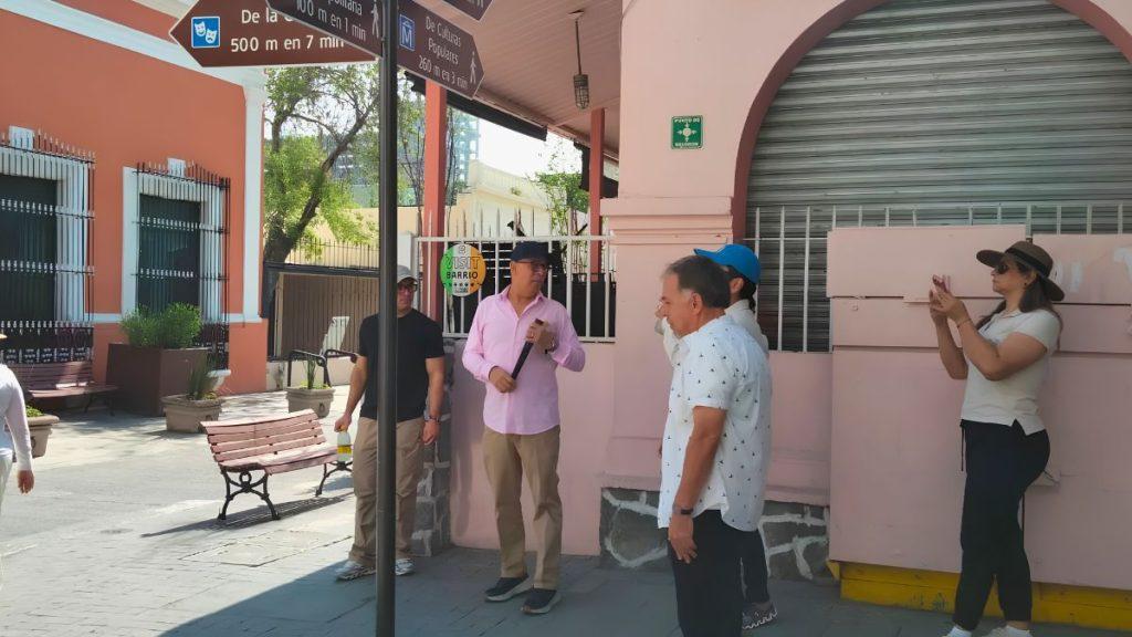 Tour group gathers in a sunny plaza beside a pink building with arches a guide with a microphone leads the conversation   Informe Regio