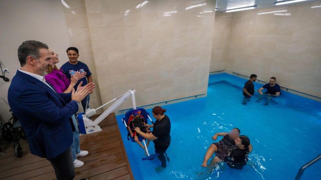 People applaud while a trainer demonstrates a water rescue device at the pool edge A person in a harness is being lowered into the water for a drill watched by others on deck and in the pool   Informe Regio
