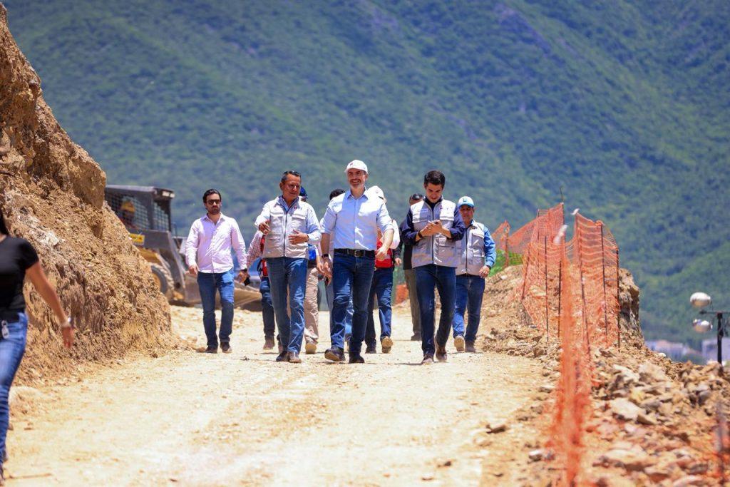 Group of men in safety vests walking along a dirt construction path with orange fencing and rocky hillside mountains in the background   Informe Regio