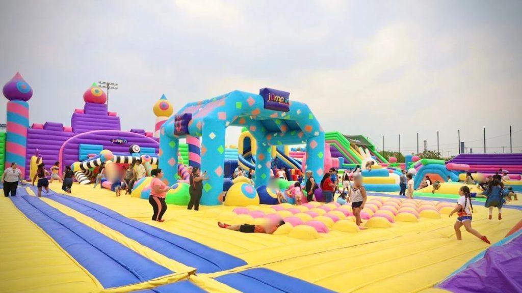 Colorful inflatable playground with slides towers and obstacles people kids and adults enjoying the outdoor park on a bright day   Informe Regio