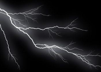White lightning bolts streak across a dark night sky with a stormy glow around them.