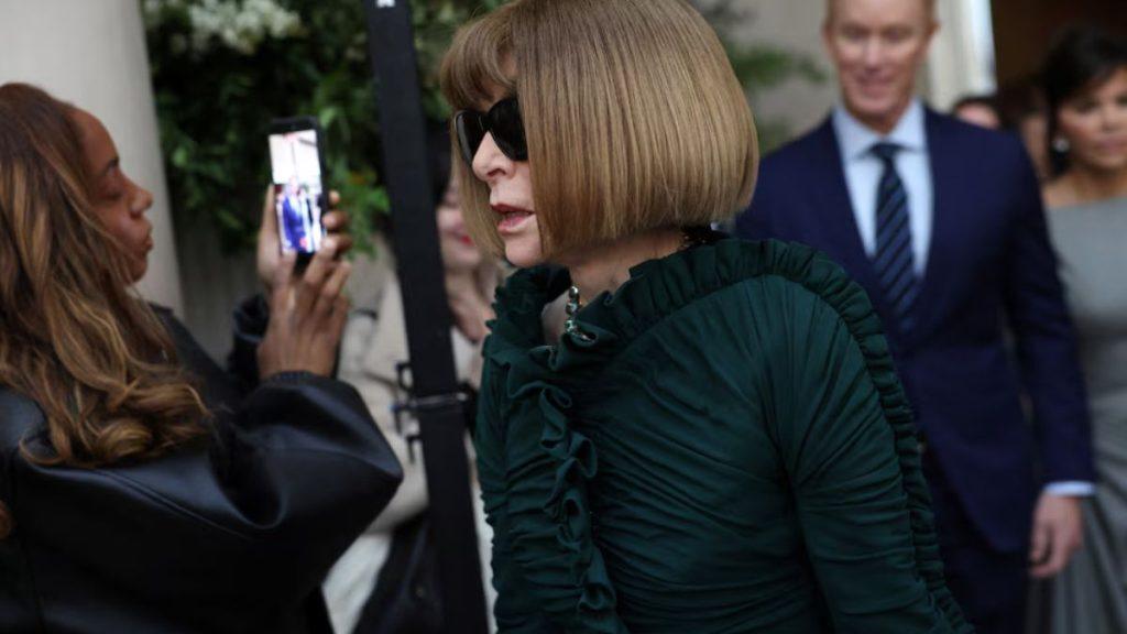 Woman with a blonde bob and dark sunglasses wearing a green ruched dress being photographed with a smartphone at a formal event   Informe Regio
