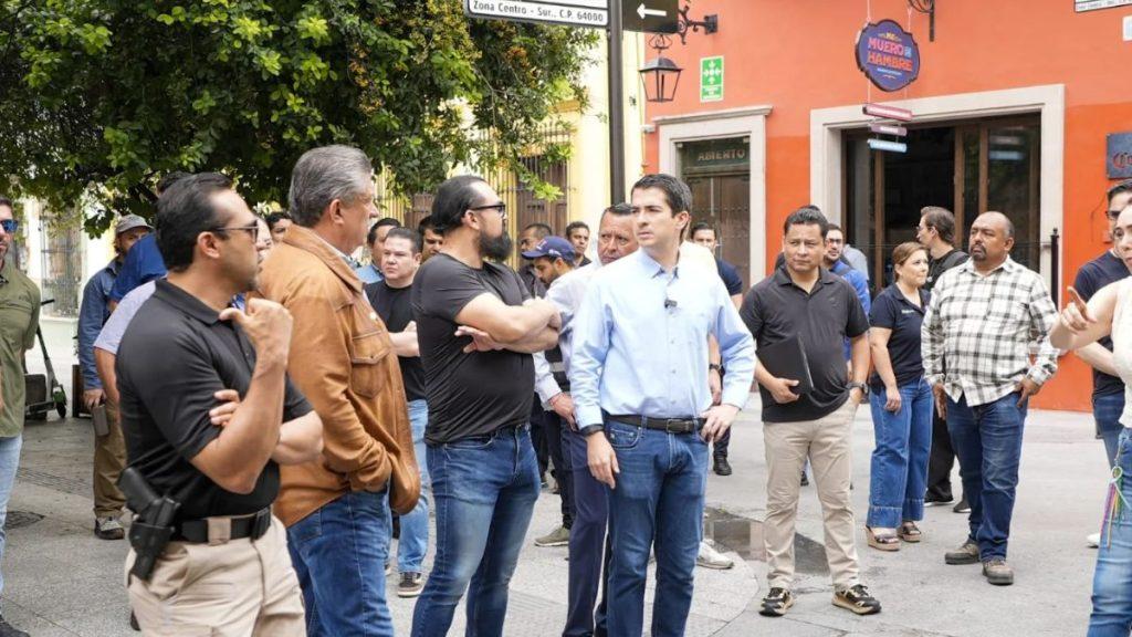A group of casually dressed people stand on a sidewalk near a bright orange building some arms crossed as if watching or waiting for something to happen   Informe Regio