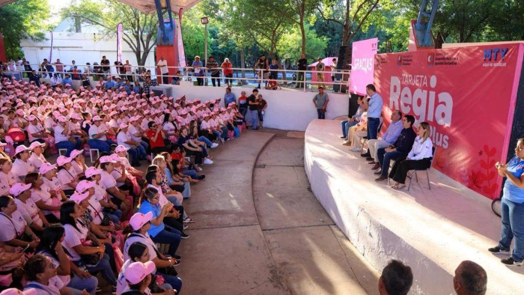 Large audience wearing pink hats seated in an outdoor amphitheater facing a pink stage with panelists and a bright banner reading Regia in the background   Informe Regio