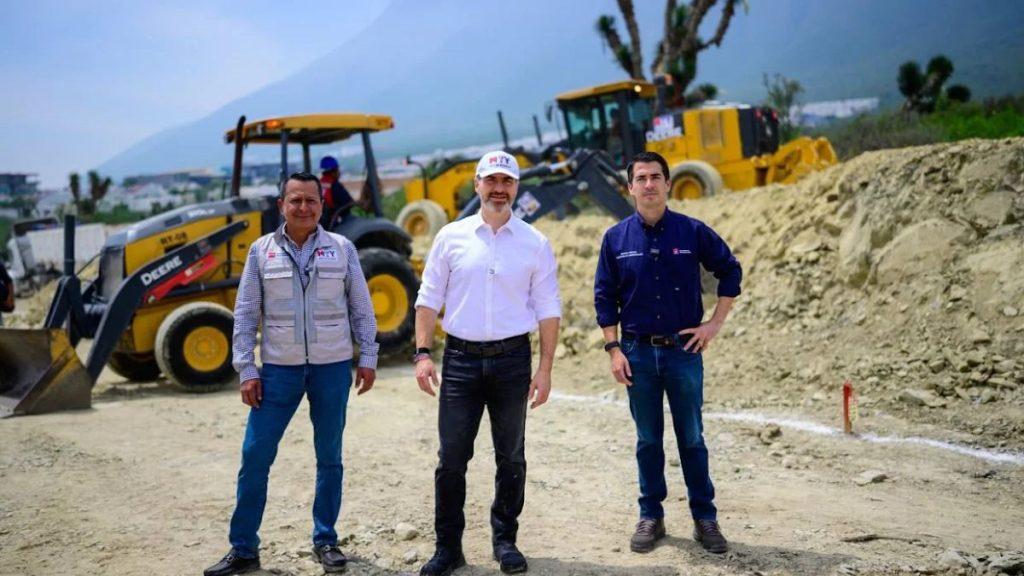 Three men stand on a dirt construction site with yellow excavators in the background posing for a photo   Informe Regio