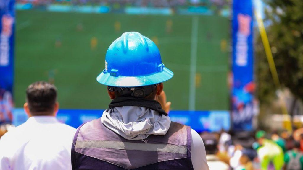 Back view of a spectator wearing a blue hard hat watching a large outdoor screen at a crowd event   Informe Regio
