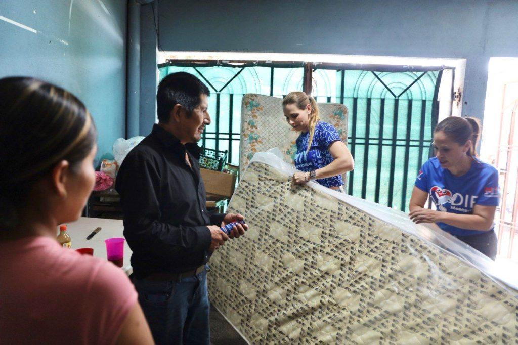 People help unload a large mattress in a blue walled room with a man in a black shirt and two women guiding the mattress from a plastic cover   Informe Regio
