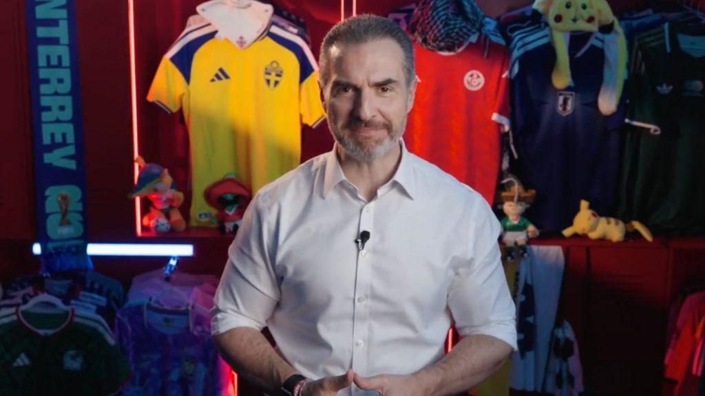 Presenter in a white shirt speaks to the camera in a studio with colorful sports jerseys and plush toys in the background   Informe Regio