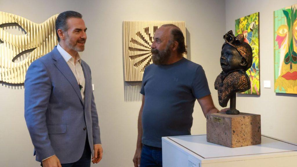 Two men converse in an art gallery beside a sculpted bust on a pedestal   Informe Regio