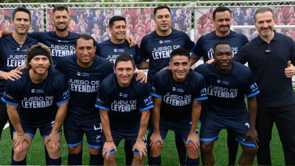 Group of soccer players in navy jerseys posing for a team photo on a green field shirts read Juego de Leyendas   Informe Regio