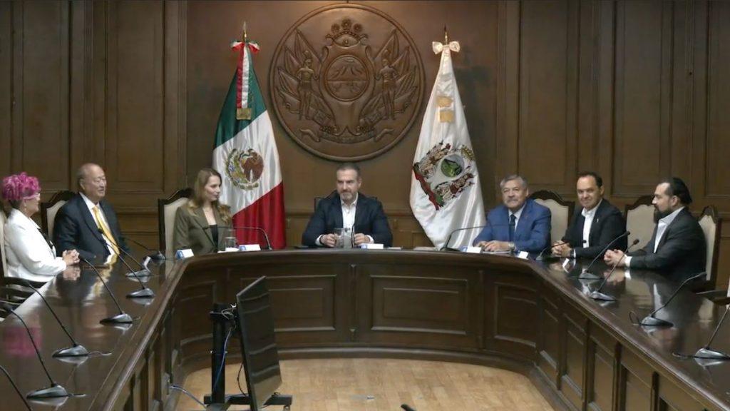 Eight officials sit around a U shaped wooden conference table in a formal meeting room Mexican flag and another flag behind them   Informe Regio