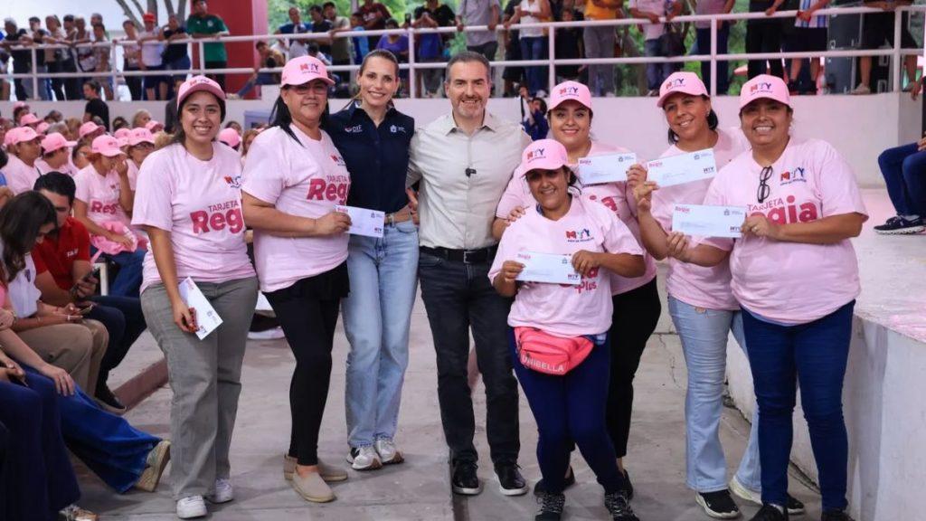 Discurso-del-alcalde-adrian-de-la-garza-sobre-las-mujeres - Informe Regio Group of smiling women in pink shirts and caps pose with a man in a gray shirt center each holding white envelopes at an outdoor event venue Informe Regio