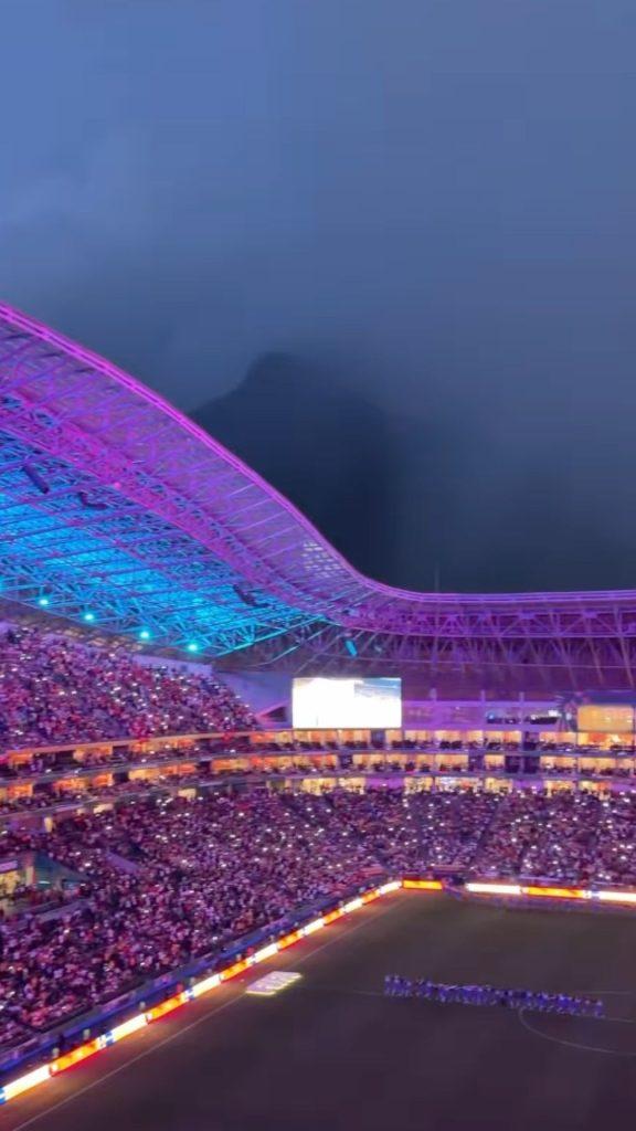 Nighttime stadium with neon pink and blue curved roof crowded stands and a lit field   Informe Regio