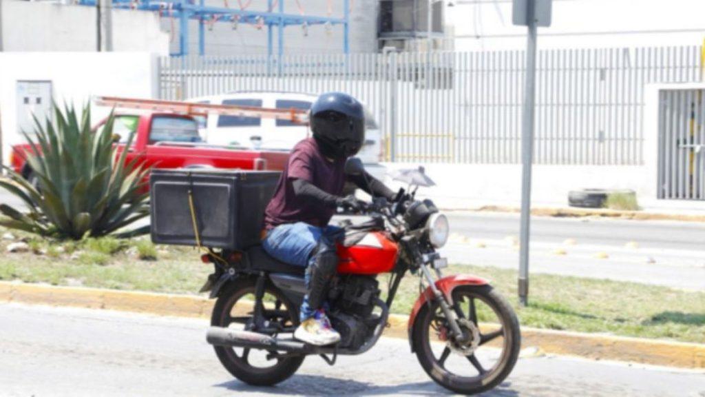 Motorcyclist wearing a helmet riding a red bike with a large storage case on a city street   Informe Regio