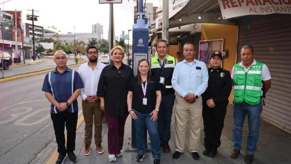 Nine people stand in a line on a city sidewalk some in uniforms with badges posing for a group photo near storefronts and a blue utility pedestal behind them   Informe Regio
