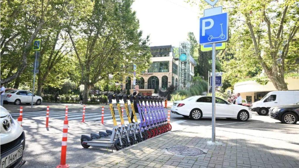 Row of colorful rental scooters lined up on a city sidewalk near a blue parking sign with trees and cars in the background   Informe Regio
