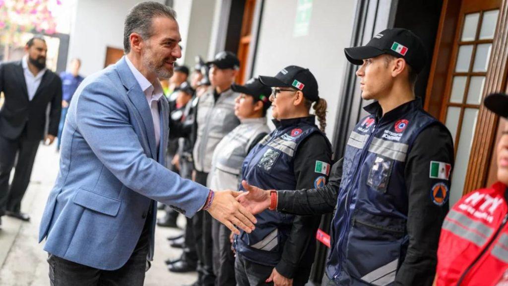 Man in a light blue blazer shakes hands with a line of uniformed responders wearing navy vests with Mexican flags outside a doorway   Informe Regio