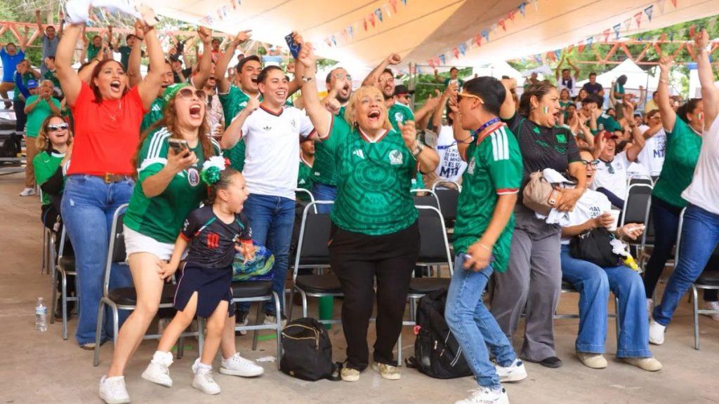 Primer-partido-de-mexico-en-el-mundial-del-2026 - Informe Regio Group of fans in green jerseys cheer with raised arms under a bunting canopy at an outdoor sports event Informe Regio