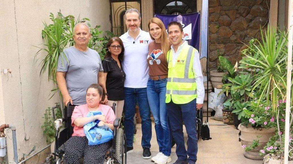 Seven people pose on a front porch outside a home a woman in a wheelchair in pink others smiling nearby with plants around and a neon safety vested volunteer in the group   Informe Regio