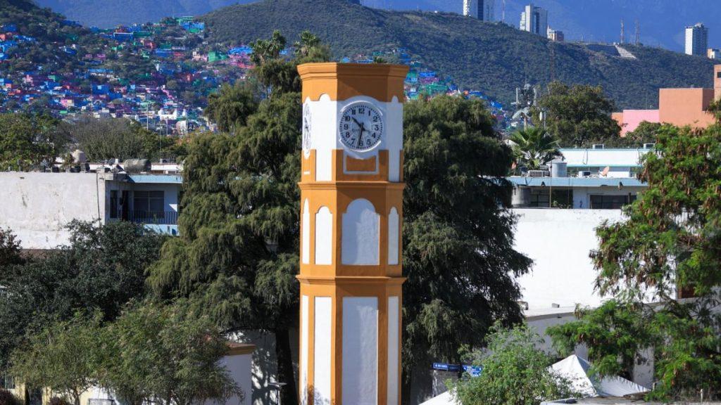 Orange and white clock tower in a city square with hills and colorful houses in the background   Informe Regio